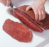 Beef being cut into slices on cutting board for preparation of beef tartare, step 1