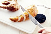 Baked chicken being cut into slices with knife and carving fork on chopping board, step 4