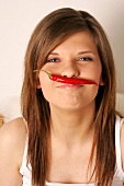 Portrait of woman with long hair holding red hot chilli pepper between nose and lip
