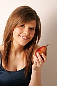 Portrait of woman with brown hair holding red pear, smiling
