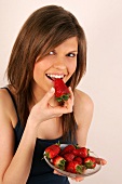 Portrait of woman with brown hair biting strawberry, smiling