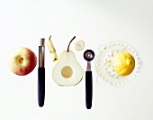 Apple, juicer, half pear without seeds, melon baller and seed remover on white background