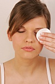 Close-up of pretty woman with brown hair cleaning her eyes with eye pad