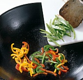 Adding vegetables to wok with slices of colourful bell peppers, step 2