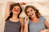 Two happy young woman lying and holding peppers in mouth and between lips and nose