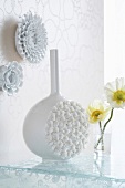 Vase mit plastischem Muster vor Wand mit Deko
