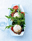 Arugula and tomato salad with goat cheese and black olives in serving dish