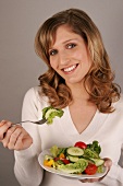 Portrait of beautiful woman with lettuce on her fork while holding salad dish, smiling