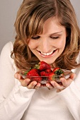 Young woman holding and looking at dish of strawberries, smiling