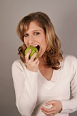 Frau mit langen Haaren beißt kräftig in Apfel