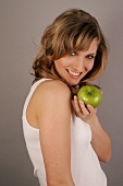 Young woman holding green apple while looking over shoulder, smiling