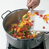 Peppers being put in casserole for preparation of consomme, step 1