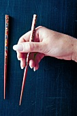 Close-up of hand holding chopstick against blue background