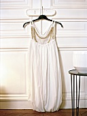 Weißes Kleid aus Seide hängt auf einem Bügel an einer Tür