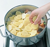 Slices of potatoes being placed on mixture in pot, step 3