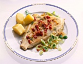 Fried plaice with small bacon pieces and potatoes on plate