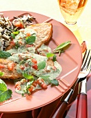 Fried boneless meat garnished with lemon sauce, tomatoes and sage on plate
