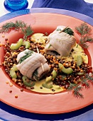 Plaice rolls garnished with lentils, cucumbers, dill herb and sauce on plate