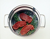 Raw meat on herbs in steam strainer on white background