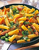 Close-up of colourful pasta dish with peas, smoked pork and herbs in pan