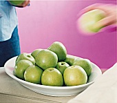 Hand greift nach grünem Apfel auf weißer Schale