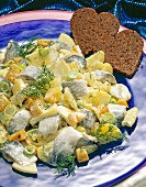 Close-up of sweet-sour herring with potato salad, dill and heart shape bread on plate