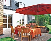 Tisch und Stühle aus Holz unter Sonnenschirm in Rot auf Terrasse