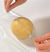 Ball of dough being covered with plastic wrap, step 2