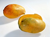 Whole and halved orange and yellow mangoes on white background