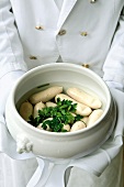 Close-up of waiter holding white sausages with parsley in porcelain bowl