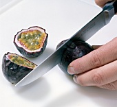 Passion fruit being cut into slices with knife and halved passion fruit, step 1