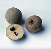 Whole and halved sapodillas on white background