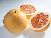 Whole and halved yellow pomelos with orange flesh on white background