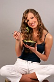Frau sitzt Schneidersitz hat Schüssel mit Salat in der Hand