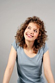 Beautiful woman with curly hair wearing gray top smiling and looking up