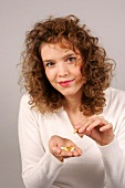 Portrait of beautiful woman with curly hair wearing white sweater holding pill, smiling