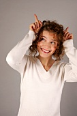 Beautiful woman with curly hair in white sweater making horns with fingers, smiling widely