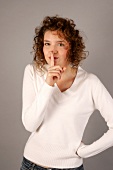 Portrait of beautiful woman with curly hair in white sweater standing with finger on lips