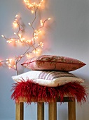 Pillow in red, beige and orange on wooden stools with lights on branch