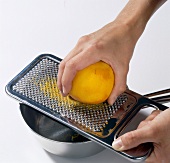 Close-up of hand peeling orange on grater