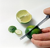 Close-up of hand cutting lime on white background