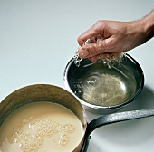 Close-up of hand adding gelatine in liquid for preparing dessert, step 1