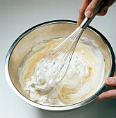Close-up of hand whisking cream in pot for preparation of dessert, step 4