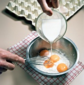 Milk being poured on flour and egg yolks in pot for preparation of dessert, step 1