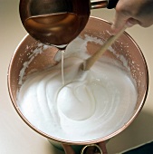 Sugar syrup being poured in cream for preparation of meringue, step 1