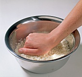 Close-up of hand kneading nishiki rice in bowl, step 1