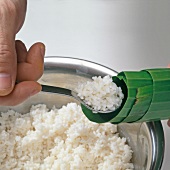 Close-up of hand filling glutinous rice in banana leaves with spoon, step 1