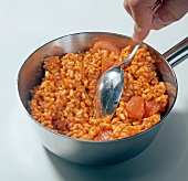 Close-up of hand mixing tomato rice with spoon in saucepan, step 1