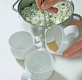 Close-up of hands basting auspinseln oil on mugs beside rice with herbs in casserole