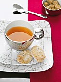 Tasse in Silber mit Tee und Kekse auf Tellern in Weiß mit Goldmuster